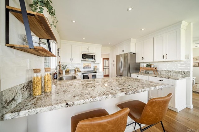 3890 Vista Campana S Unit 35, Oceanside, CA 92057 - kitchen with appliances with stainless steel finishes, a sink, a peninsula, open shelves, and light wood-type flooring