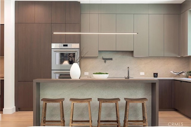 4625 Vesper Ave, Sherman Oaks, CA 91403 - kitchen featuring stainless steel double oven, light wood finished floors, a kitchen breakfast bar, tasteful backsplash, and a sink