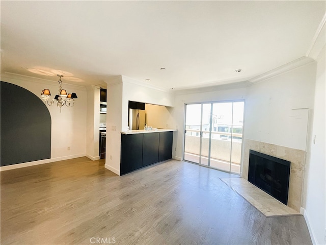 10960 Ashton Ave Unit 307, Los Angeles, CA 90024 - unfurnished living room with a chandelier, crown molding, light wood-style floors, a tiled fireplace, and arched walkways