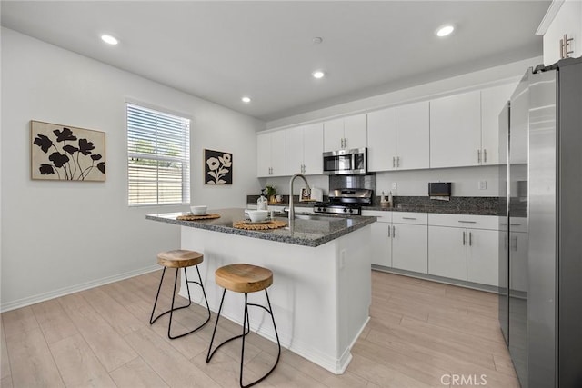 2544 Gunner Ridge Way, Rialto, CA 92377 - kitchen with stainless steel appliances, light wood-type flooring, white cabinets, a breakfast bar, and a kitchen island with sink