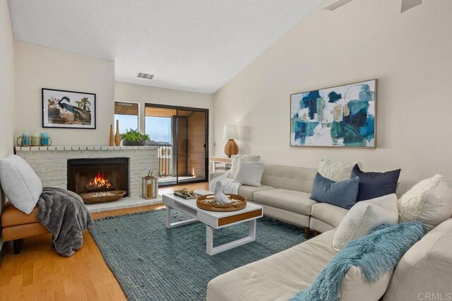 801 Kalpati Cir Unit B, Carlsbad, CA 92008 - living area featuring wood finished floors, lofted ceiling, a brick fireplace, and a textured ceiling
