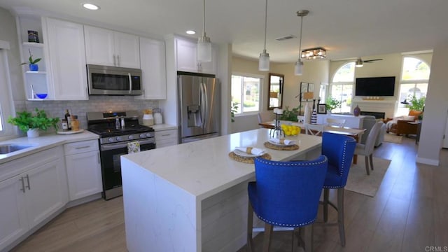 13356 Corte De Chucena, San Diego, CA 92128 - kitchen featuring stainless steel appliances, a kitchen island, white cabinetry, light wood-style floors, and decorative backsplash