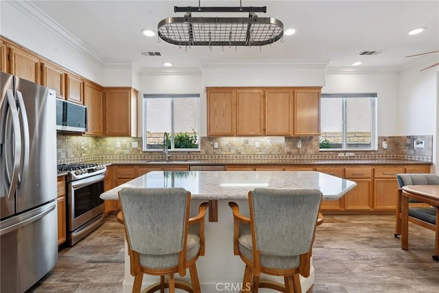 19613 Edmonds Pl, Saugus, CA 91350 - kitchen with appliances with stainless steel finishes, a kitchen island, crown molding, light stone counters, and a breakfast bar