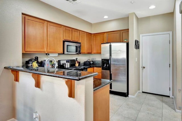 4300 Newton Ave Unit 110, San Diego, CA 92113 - kitchen with stainless steel appliances, a peninsula, brown cabinetry, dark stone counters, and a breakfast bar