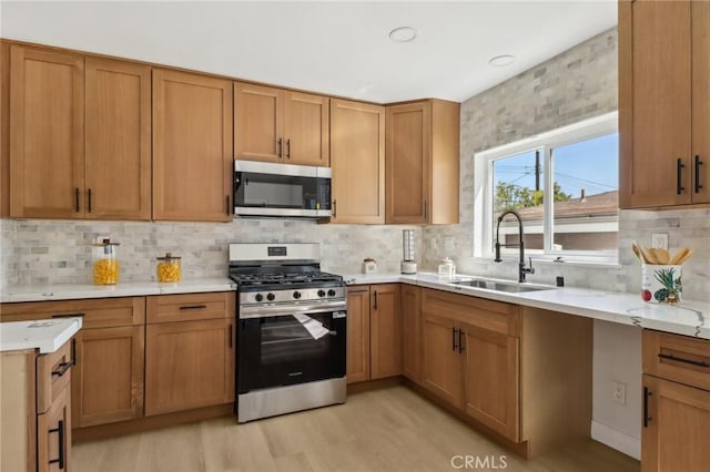 12548 Terra Bella St, Pacoima, CA 91331 - kitchen featuring stainless steel appliances, a sink, light wood-style floors, tasteful backsplash, and brown cabinets