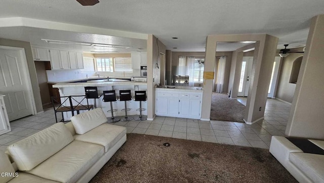 12780 Fir St, Oak Hills, CA 92344 - living area featuring light carpet, light tile patterned floors, ceiling fan, baseboards, and a textured ceiling