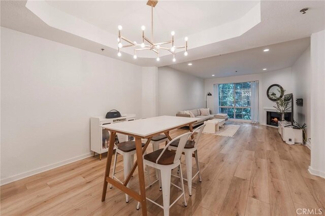 585 N Rossmore Ave Unit 209, Los Angeles, CA 90004 - dining room with a tray ceiling, light wood-type flooring, baseboards, a lit fireplace, and a chandelier