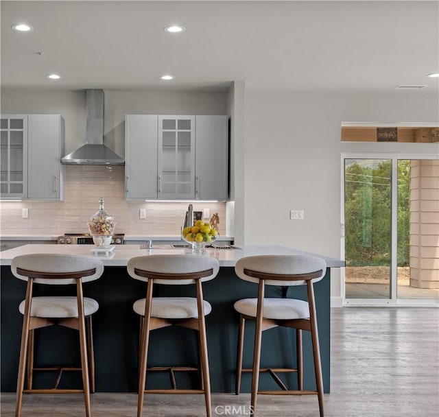 29300 Horsethief Dr, Tehachapi, CA 93561 - kitchen featuring wall chimney range hood, gray cabinets, light countertops, backsplash, and a kitchen bar