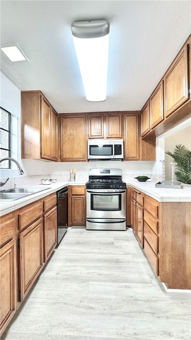 2971 Plaza Del Amo Unit 243, Torrance, CA 90503 - kitchen with appliances with stainless steel finishes, light wood-style floors, a sink, and brown cabinetry