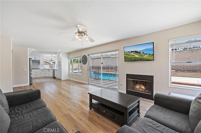 2251 Via Pacifica, Corona, CA 92882 - living area featuring a glass covered fireplace, ceiling fan, light wood-style flooring, and baseboards