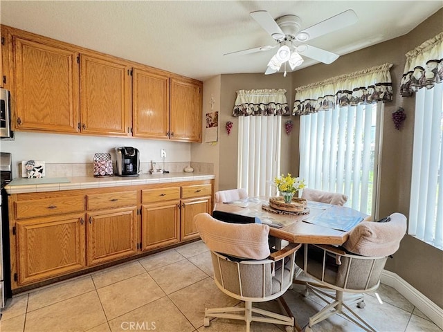30027 Via Amante, Menifee, CA 92584 - kitchen featuring stainless steel microwave, light tile patterned floors, ceiling fan, tile countertops, and brown cabinetry