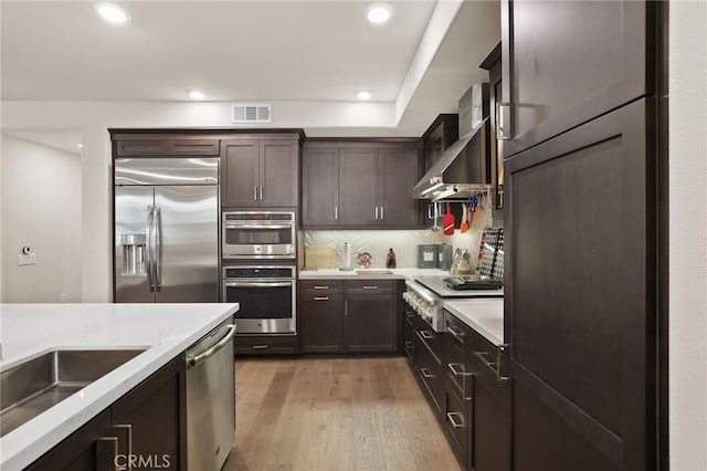 223 Carlow, Irvine, CA 92618 - kitchen with appliances with stainless steel finishes, dark brown cabinets, light countertops, wall chimney range hood, and light wood finished floors