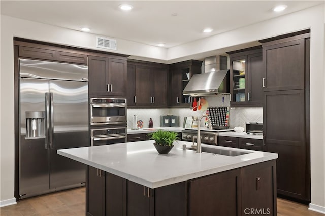 223 Carlow, Irvine, CA 92618 - kitchen featuring stainless steel appliances, wall chimney range hood, dark brown cabinets, backsplash, and recessed lighting