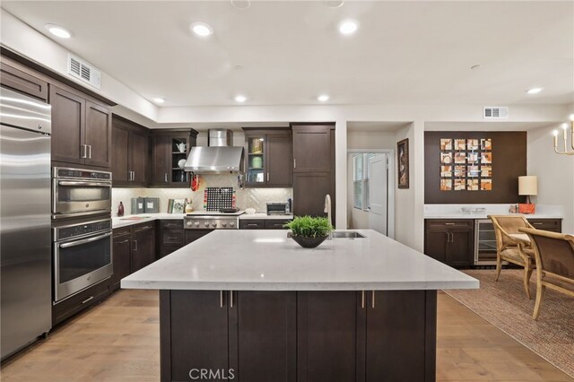 223 Carlow, Irvine, CA 92618 - kitchen featuring wall chimney range hood, appliances with stainless steel finishes, a sink, dark brown cabinetry, and tasteful backsplash