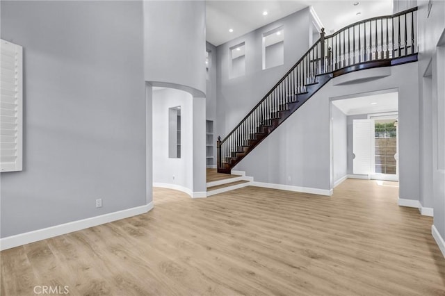 23922 Lakeside Rd, Valencia, CA 91355 - unfurnished living room featuring baseboards, stairs, wood finished floors, arched walkways, and a high ceiling