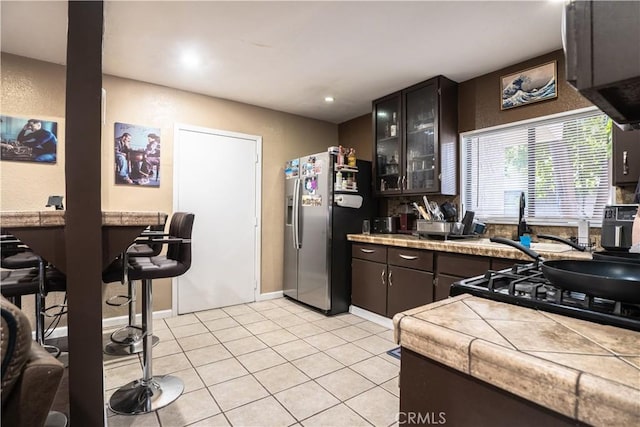 11737 Bellman Ave, Downey, CA 90241 - kitchen featuring stainless steel refrigerator with ice dispenser, glass insert cabinets, light tile patterned floors, tile counters, and dark brown cabinetry
