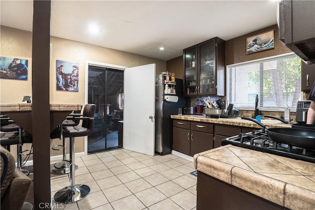 11737 Bellman Ave, Downey, CA 90241 - kitchen with glass insert cabinets, dark brown cabinets, light tile patterned floors, exhaust hood, and freestanding refrigerator
