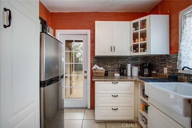 6155 Cahuilla Ave Unit 29, Palms, CA 92277 - kitchen featuring freestanding refrigerator, light tile patterned floors, white cabinetry, glass insert cabinets, and decorative backsplash