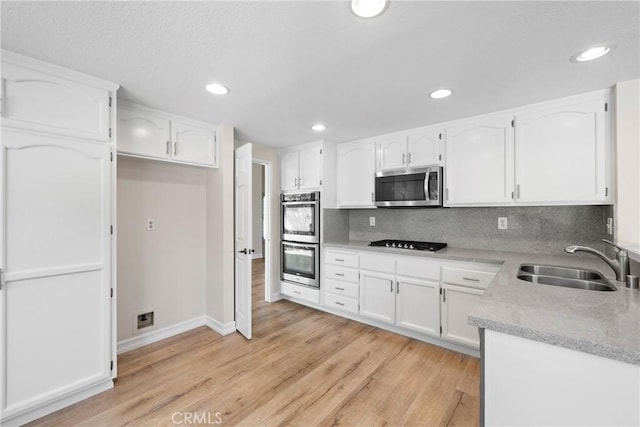 3 Andria, Irvine, CA 92614 - kitchen featuring appliances with stainless steel finishes, a sink, white cabinetry, light wood-style flooring, and backsplash