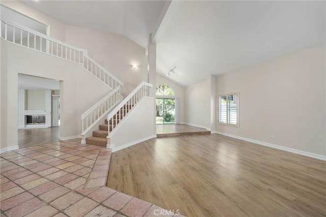 3 Andria, Irvine, CA 92614 - unfurnished living room with stairway, baseboards, a brick fireplace, wood finished floors, and high vaulted ceiling