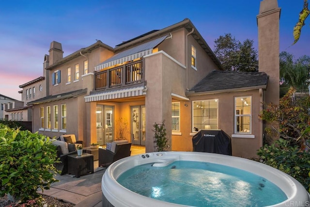 2386 Lapis Rd, Carlsbad, CA 92009 - back of house at dusk with a balcony, a hot tub, stucco siding, and a chimney