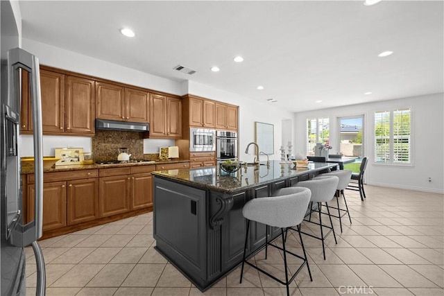 26865 Grey Pl, Stevenson Ranch, CA 91381 - kitchen with appliances with stainless steel finishes, light tile patterned flooring, recessed lighting, dark stone countertops, and brown cabinetry