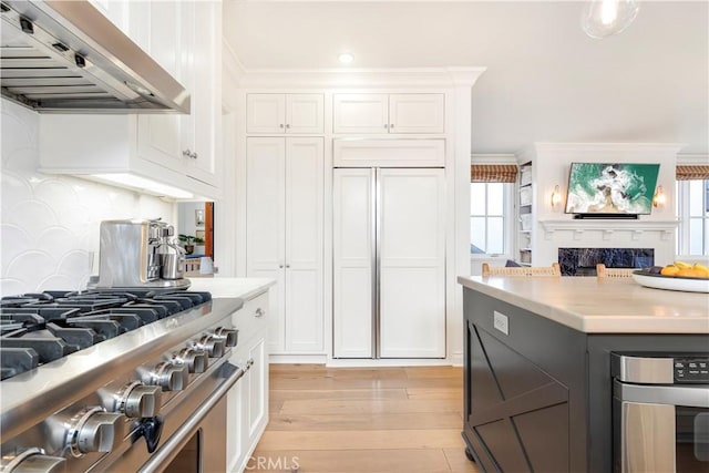 7161/2 Iris Ave, Corona Del Mar, CA 92625 - kitchen featuring wall chimney range hood, high end range, light countertops, white cabinets, and light wood-style floors