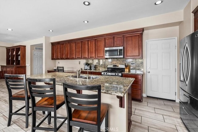 27109 Woodglen Ln, Moreno Valley, CA 92555 - kitchen featuring appliances with stainless steel finishes, a sink, a center island with sink, stone counters, and a kitchen breakfast bar