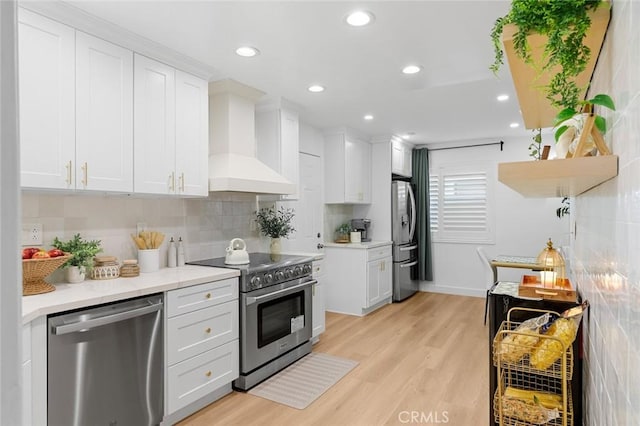 16782 Heritage Ln, Huntington Beach, CA 92647 - kitchen featuring stainless steel appliances, wall chimney range hood, light wood-style flooring, white cabinetry, and tasteful backsplash