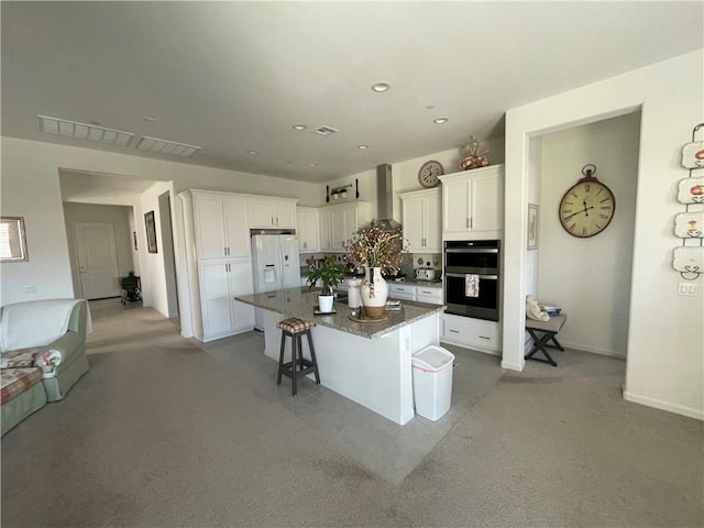 11915 Sagecrest Ct, Corona, CA 92883 - kitchen featuring wall chimney exhaust hood, white cabinets, a kitchen breakfast bar, dark stone counters, and a center island