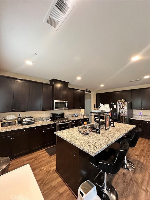 36569 Olea Ct, Beaumont, CA 92223 - kitchen with appliances with stainless steel finishes, a kitchen bar, light wood finished floors, light stone counters, and an island with sink