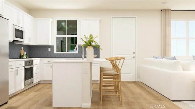2557 E Hyde Paseo, Ontario, CA 91762 - kitchen featuring white microwave, stainless steel oven, light wood-style floors, decorative backsplash, and a kitchen island with sink