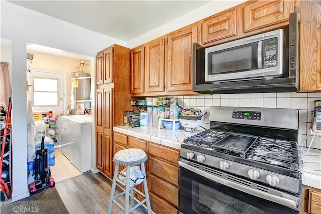 18003 Saticoy St, Reseda, CA 91335 - kitchen with stainless steel appliances, backsplash, light wood-type flooring, brown cabinetry, and tile counters