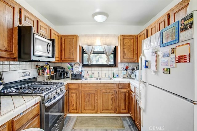18003 Saticoy St, Reseda, CA 91335 - kitchen featuring appliances with stainless steel finishes, tile counters, a sink, tasteful backsplash, and brown cabinets