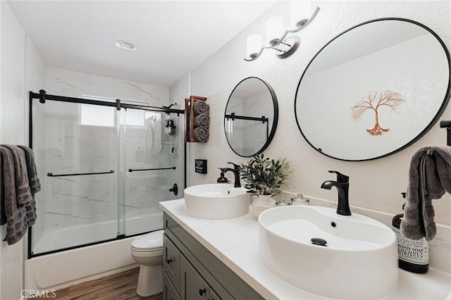 26625 Pinehurst Dr, Lake Arrowhead, CA 92352 - full bath with combined bath / shower with glass door, a textured wall, double vanity, toilet, and wood finished floors