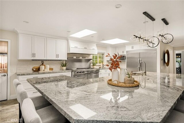 20402 Seven Seas Ln, Huntington Beach, CA 92646 - kitchen featuring high quality appliances, custom exhaust hood, a breakfast bar, tasteful backsplash, and white cabinetry