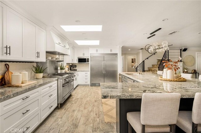 20402 Seven Seas Ln, Huntington Beach, CA 92646 - kitchen featuring premium appliances, light wood-style flooring, a breakfast bar, white cabinetry, and tasteful backsplash