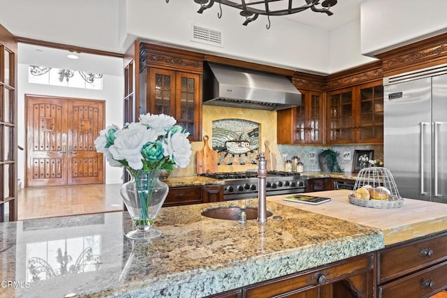 13045 Ripple Creek Ln, Camarillo, CA 93012 - kitchen with wall chimney range hood, light stone countertops, tasteful backsplash, glass insert cabinets, and range