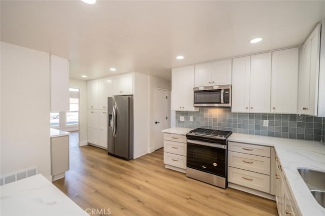 40033 Sagewood Dr, Palm Desert, CA 92260 - kitchen featuring appliances with stainless steel finishes, light stone counters, tasteful backsplash, white cabinetry, and light wood-style flooring