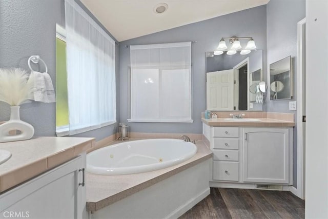 8510 Verdant Ct, Los Molinos, CA 96055 - bathroom featuring two vanities, vaulted ceiling, a tub with jets, and wood finished floors