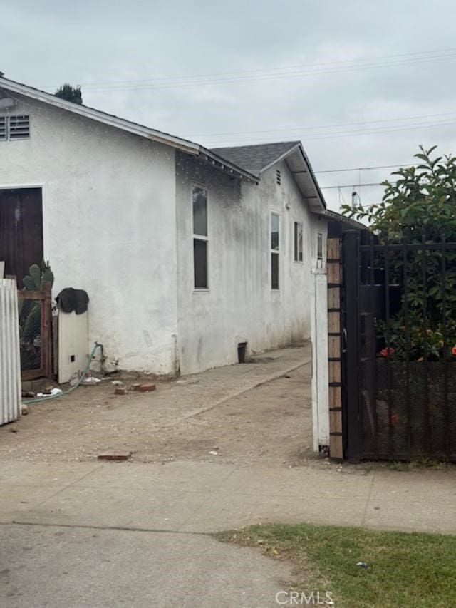 3815 Paloma St, Los Angeles, CA 90011 - view of side of home featuring a shingled roof, stucco siding, and a gate