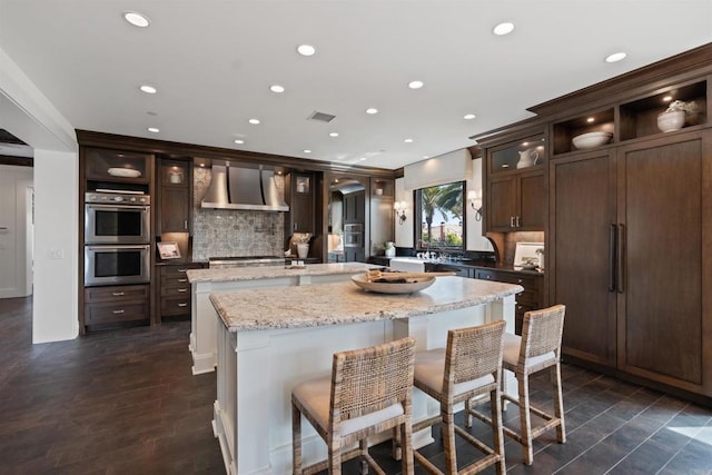 2574 Muirfields Dr, Carlsbad, CA 92009 - kitchen with wall chimney range hood, a kitchen island, double oven, tasteful backsplash, and dark brown cabinets