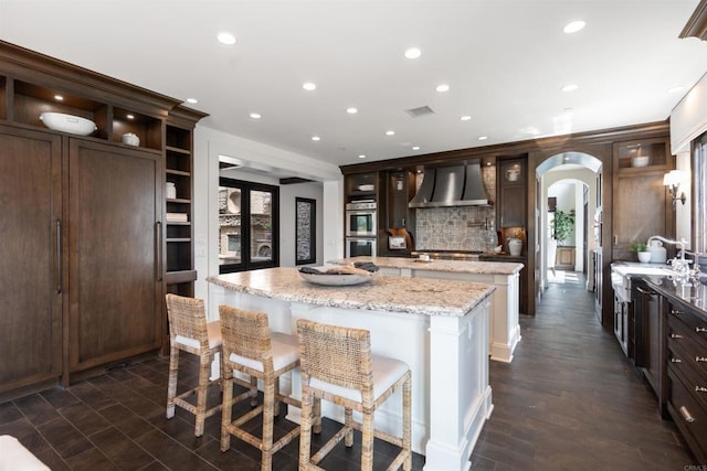2574 Muirfields Dr, Carlsbad, CA 92009 - kitchen featuring wall chimney exhaust hood, a kitchen island, appliances with stainless steel finishes, arched walkways, and a sink