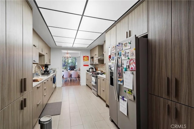 241 S Reeves Dr Unit 302, Beverly Hills, CA 90212 - kitchen featuring appliances with stainless steel finishes, light countertops, under cabinet range hood, backsplash, and a chandelier