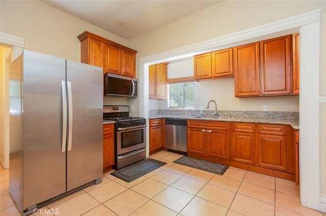 2712 Kenwood Ave, Los Angeles, CA 90007 - kitchen with stainless steel appliances, a sink, light stone counters, brown cabinets, and light tile patterned floors