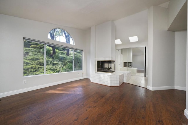 1688 Crystal Ridge Ct, Vista, CA 92081 - unfurnished living room with a tiled fireplace, baseboards, a skylight, wood finished floors, and a high ceiling