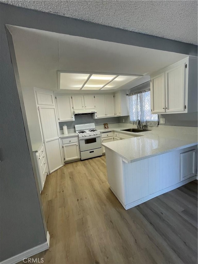 14199 Havasu Rd, Apple Valley, CA 92307 - kitchen featuring white gas stove, a peninsula, light wood-style floors, light countertops, and under cabinet range hood