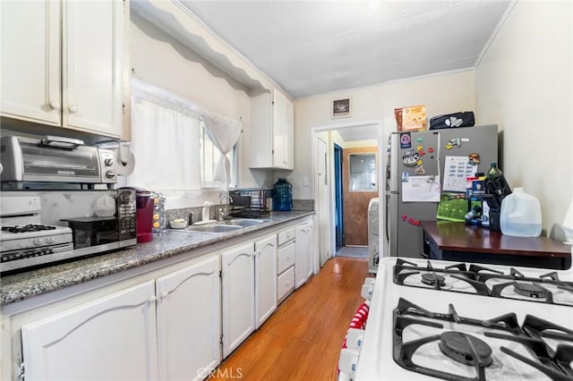 151 E 105th St, Los Angeles, CA 90003 - kitchen featuring a sink, light wood-style flooring, white cabinets, white range with gas cooktop, and freestanding refrigerator