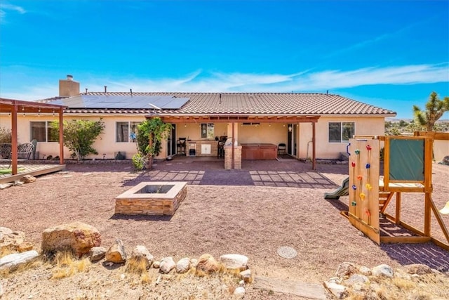 5115 Warren Vista Ave, Yucca Valley, CA 92284 - rear view of house featuring a jacuzzi, a patio area, solar panels, an outdoor fire pit, and a chimney