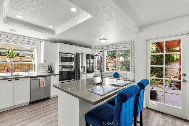19777 Azure Field Dr, Newhall, CA 91321 - kitchen featuring stainless steel appliances, a textured ceiling, light wood-style flooring, a kitchen breakfast bar, and white cabinets